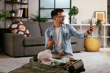 Fototapeta premium Young smiling man packing clothes into travel bag. Man preparing for the trip