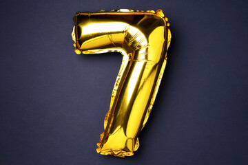 Creative layout. Golden foil balloon number and digit seven 7. Birthday greeting card. Anniversary concept. Top view. Copy space. Stylish gold numeral over black background. Numerical digit.