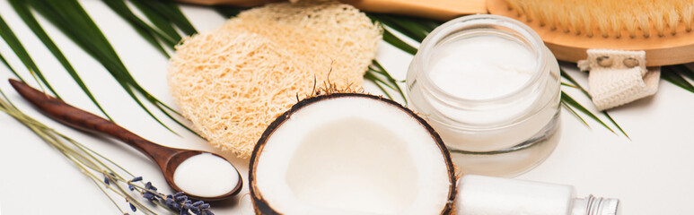 half of coconut, cosmetic cream, sponges and lavender twigs with palm leaves on white, 
