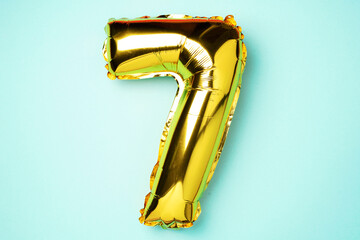 Creative layout. Golden foil balloon number and digit seven 7. Birthday greeting card. Anniversary concept. Top view. Copy space. Stylish gold numeral over blue background. Numerical digit.
