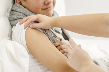 A sick boy is given a shot in the forearm during treatment. An unhealthy child at home. Cold season.