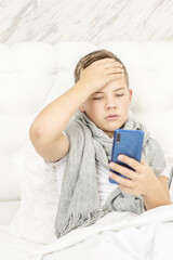 Sick teen boy makes a video call to the doctor during illness at home with a thermometer in his mouth.  Cold season.