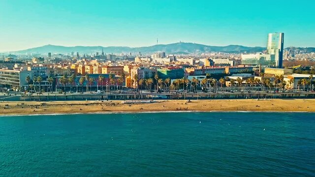 Drone footage of the promenade at La Barceloneta beach with the cityscape in the background. 