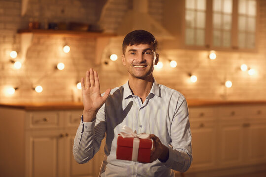 Happy man holding present box and greeting girlfriend online during online meeting