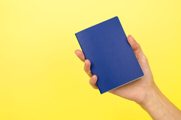 Blue passport without inscriptions in a female hand on a yellow background