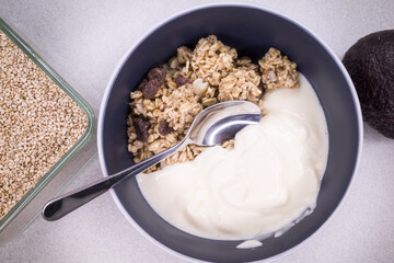 A bowl of granola with yogurt an avocado and sesame seeds.
