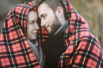 Fototapeta premium A young couple in love is covered with a red blanket on their head and looks at each other. Outside. Portrait, close-up. The concept of love, happiness, and romantic relationships. Valentine's day.