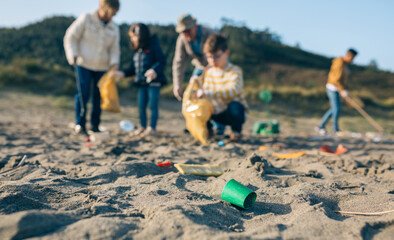 Group of volunteers picking up trash on the beach. Selective focus on plastic lid in foreground