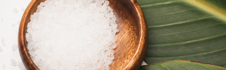 Close up view of natural sea salt in wooden bowl on green leaf, - Powered by Adobe