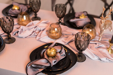 Close up of festive Christmas table setting with empty wine glasses and black plate with gold garnet
