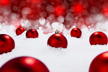 Shiny red Christmas baubles in stick in snow with beautiful red and with bokeh in background