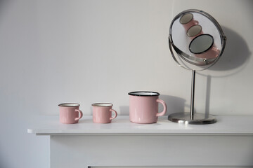 Three small pink pastel coffee cups on a white console against a wall background.