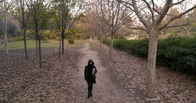 mujer camina por sendero de bosque en oto&ntilde;o con capucha y mascarilla pandemia