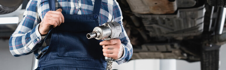 cropped of mechanic holding pneumatic wrench on blurred background, banner