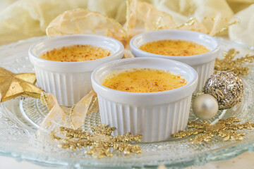 Creme brulee - traditional french vanilla cream dessert with caramelised sugar on top. Three servings served on a decorated glass plate with a golden Christmas decoration.