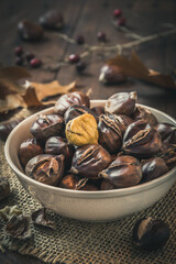 Roasted chestnuts in a bowl, one peeled, on a dark wooden background, vertical