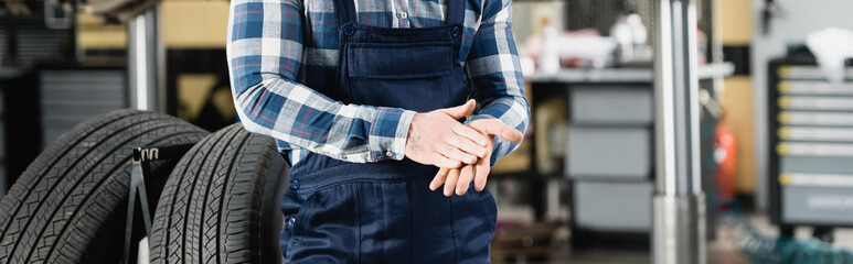 partial view of repairman rubbing hands while standing near car wheels in garage, stock image