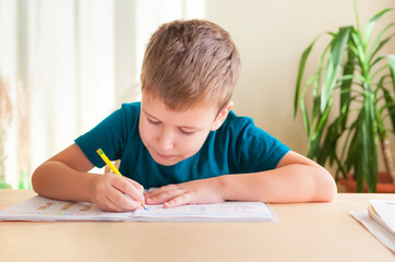 7 years old child boy studying lessons sitting at desk in his room.