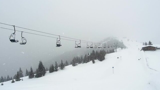 Empty ski lift in snowfall. Chairlifts move under snow storm in mountains ski resort Zell am See Kaprun, Austria. Snowy forest in background. Austrian Alps during bad winter weather, poor visibility
