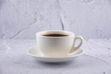 One white cup with aroma refreshing coffee on white plaster background.
