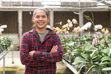 Portrait of young man Asian farmer smiling and arms crossed in Phalaenopsis orchid greenhouse
