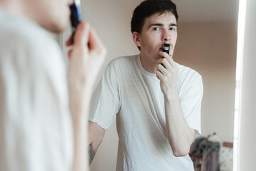 teenager shaves stubble with an electric razor, zerkolo rejection, personal care, man with black...