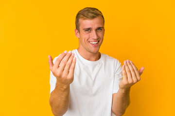 Young caucasian handsome man pointing with finger at you as if inviting come closer.