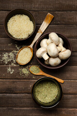 Vertical image.Ceramic bowls full of rice and dried rosemary, mushrooms, wooden spoons on the rusic brown table