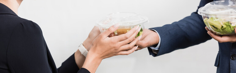 Cropped view of businesswoman taking plastic bowl with meal from colleague on white, 