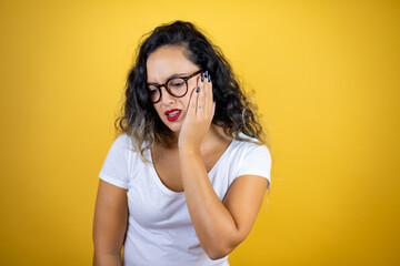 Young beautiful woman wearing casual white t-shirt over isolated yellow background touching mouth with hand with painful expression because of toothache or dental illness on teeth