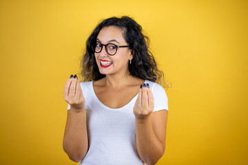 Young beautiful woman wearing casual white t-shirt over isolated yellow background doing money gesture with hands, asking for salary payment, millionaire business