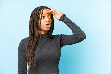 Young african american woman isolated on blue background looking far away keeping hand on forehead.