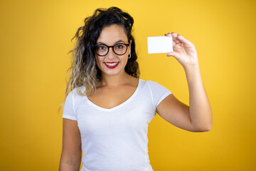 Young beautiful woman wearing casual white t-shirt over isolated yellow background smiling and holding white card