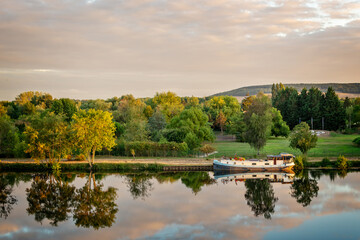 Cruise boat on the Yonne river with reflections at sunset near Joigny, Burgundy landscape, France.