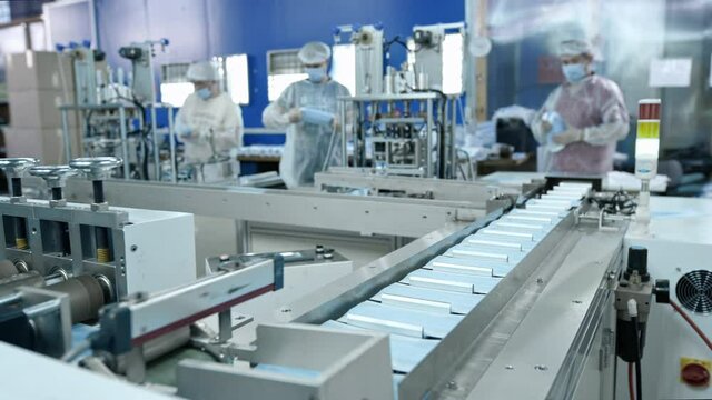 A group of workers from a factory for the production of protective medical masks. Face masks are packed in plastic bags. Machine for creating protective equipment against coronavirus or covid-19.