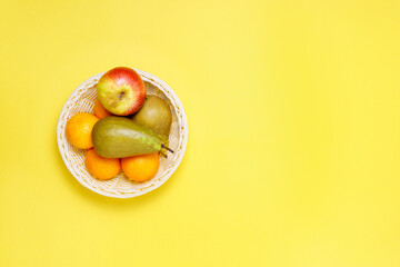 fresh fruit in a basket apples tangerines and pears on a yellow background top view. flat lay. copy space