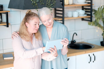 Woman teaching senior mother to use internet at home. Senior woman with her daughter looking at modern gadget indoors. relaxing together, different generations hobby pastime. support for the elderly