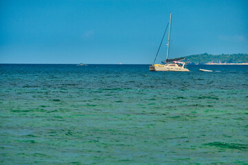 Obraz premium Philippines, Boracay island, Puka Beach. A white yacht is moored in the sea with a white rubber boat attached. Against the background of the mountain and palm trees of the neighboring island.