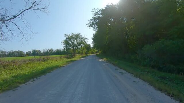 POV driving on a country gravel road past maturing fields and trees in rural Iowa on a sunny late summer day - Kalona, Iowa