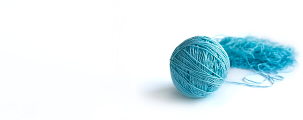 A ball of blue fine cotton yarn in the process of winding, isolated on the white background. Tangled yarn in the background. Long banner with space for text on the left.