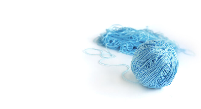 A ball of blue fine cotton yarn in the process of winding, isolated on the white background. Tangled yarn in the background. Banner with space for text on the left.