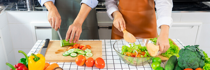 Happy couple having fun standing in kitchen at home preparing vegetable salad husband and wife vegetarians chop vegetables prepare for dinner in loft kitchen at home.