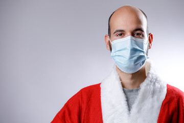 Uomo calvo con mascherina chirurgica e giacca di babbo natale guarda serio, isolato su sfondo bianco