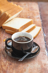 A cup of coffee with bread over a wooden rustic table.