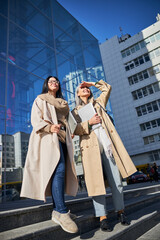 Joyful female friends with laptops standing on the street