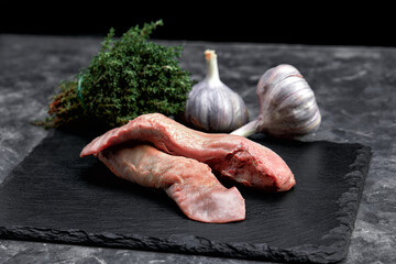 Raw beef or pork tongue with vegetables- celery, pepper, garlic, onion, lies on a cutting board, on a black background close-up © Georgii