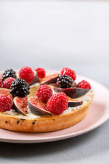 Bagel with cream cheese, figs, raspberries, blackberries and honey.  Close-up of gourmet sandwich on pink plate on gray background.