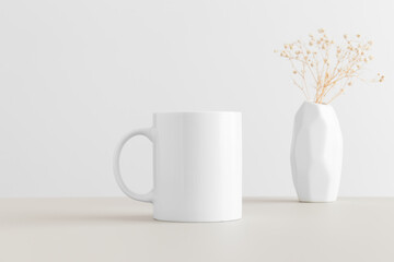 White mug mockup with a gypsophila in a vase on a beige table.