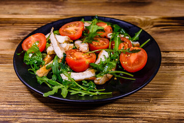 Roasted chicken breasts and salad with arugula and cherry tomatoes in a black plate