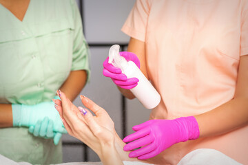 Beautician in rubber protective gloves disinfects hands of woman with antiseptic spray in a beauty salon